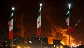 Iranian flags fly as fire and smoke from an Israeli attack on Sharan Oil depot rise. Photo: Council on Foreign Relations
