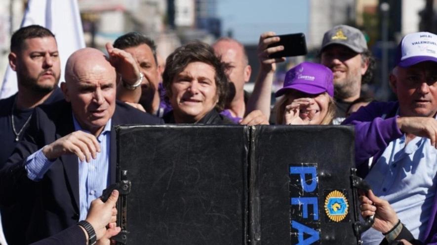 Una maleta es sostenida frente al presidente argentino Javier Milei mientras los manifestantes lanzan botellas y piedras contra el vehículo. Foto: reddit